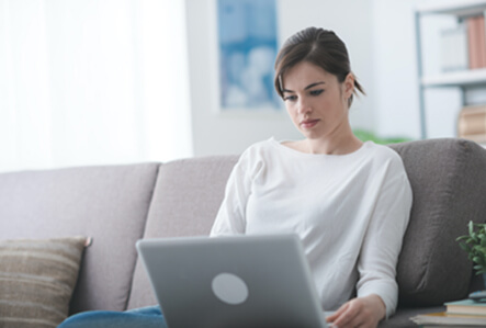 Junge Frau am Laptop beim Selbststudium auf dem Sofa